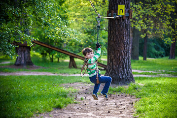 Fototapeta premium smiling boy rides a zip line. happy child on the zip line. The kid passes the rope obstacle course