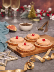 Obraz na płótnie Canvas A French traditional foie gras topped on toaster bread on a wooden plate aside with onion marmalade and a piece of fig fruit, glasses of Champagne in background, with Christmas atmosphere decoration.