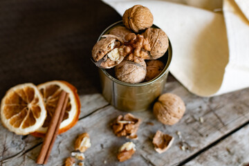 Walnuts in a tin of yellow metal next to the shell and the nuts on the inside. Decorated with dried oranges and a cinnamon stick. Composition of products and food on a wooden Board