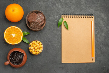Horizontal view of set of whole and cut in half fresh oranges and biscuits and notebook with pen