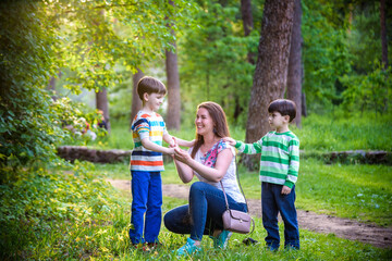 Fototapeta premium Young woman mother applying insect repellent to her two son before forest hike beautiful summer day or evening. Protecting children from biting insects at summer. Active leisure with kids