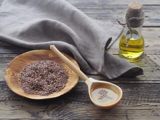 Flaxseed oil in a wooden spoon, linseeds in a wooden plate and oil in a bottle   with a linen napkin on a wooden background, top view. Natural healthy oleum lini with omega and vitamins for diets