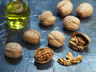 Juglans regia fruit and walnut oil in a bottle on a dark background, closeup. Healthy delicacy oil and walnut kernels with vitamins, antioxidants and omega for proper nutrition