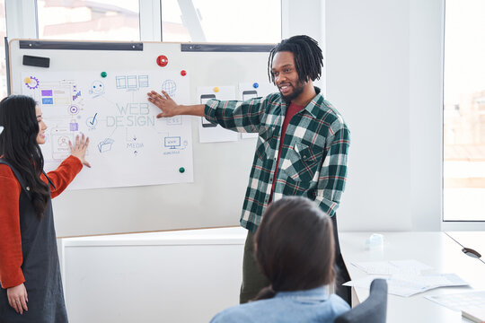Smiling multiracial student man standing near flip chart for drawing graphic