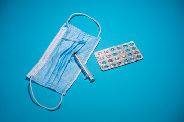 Blue face mask, pills, syringe on blue background. Medicine and healthcare. Medications and pharmacy.
