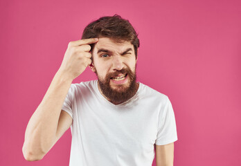 An angry man touches his head with his hands on a pink background Copy Space