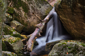Autumn long exposure of creek Black (Big) Stolpich waterfalls in Jizera Mountain. Water falls into a deep forest canyon full of granite stones and rocks covered with green moss. Czech Republic