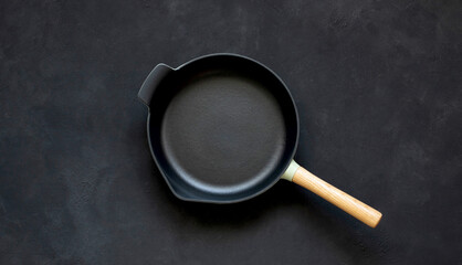 Cast iron frying pan with wooden handle on black background.