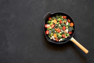 Cast iron frying pan with vegetables, spices and herbs on a black background.