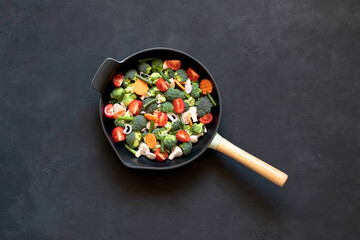 Cast iron frying pan with vegetables, spices and herbs on a black background.