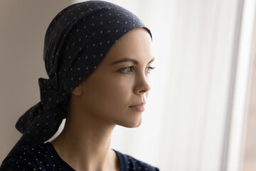 Thoughtful young woman losing hair as result of chemotherapy stand by window ponder. Serious...