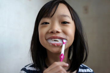 Portrait of little Asian girl brushing teeth at the bathroom