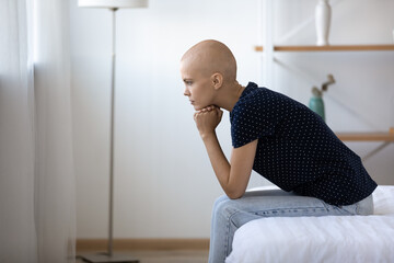 Side shot of serious pensive young woman with bald head sit on bed at home in clinic ponder on...