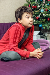 a child with a surprised face sits on the sofa under the christmas tree