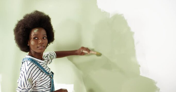 Close up of beautiful young African American woman painting wall in new apartment using paintbrush tired from work reparing home House redecoration and home construction while renovating and improving