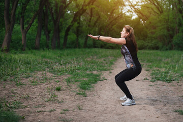 Pretty woman squats in the park, warms up before jogging in nature outdoors, a woman confidently looks ahead and knows what will be healthy after squats and jogging