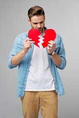 Fototapeta premium handsome young man holding broken paper red valentine heart standing over grey background