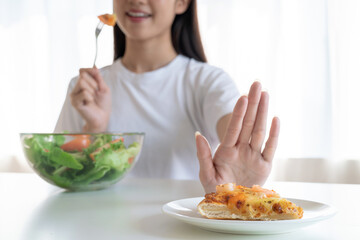 Young Asian woman pushes her favorite pizza with her hand and choose to eat a healthy vegetable salad.