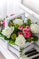 White wooden box with bouquet white and pink roses and chrysanthemums on white piano. Decoration of home. Flowers boxes. Wedding decoration