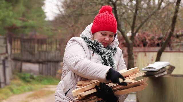 A girl in a red cap lays out chopped sticks in her hands close-up. Preparing firewood for lighting the stove. The first snow fell. New year holiday is coming soon. Warm soft light. 4K.