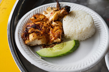 Grilled chicken served with plain white rice and cucumber on a polystyrene plate. Healthy menu.