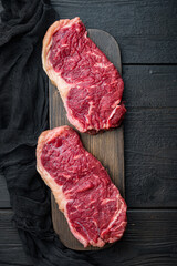 Short loin raw beef steak, on black wooden background, top view