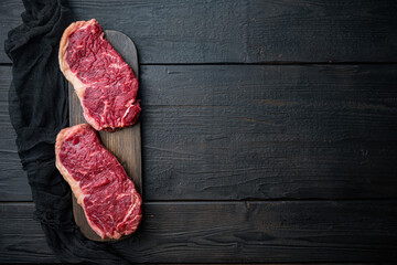 Strip loin steak, raw marbled meat, on black wooden table, top view, with copy space for text