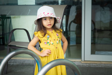 Portrait of beautiful little gorgeus lovely toddler girl in mustard summer look clothes, fashion dress, and hat. Happy healthy asian child posing in outdoor.