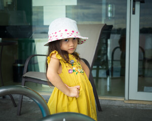 Portrait of beautiful little gorgeous lovely toddler girl in mustard summer look clothes, fashion dress, and hat. Happy healthy Asian child posing in outdoor.