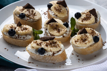 Banana and chocolate bruschetta, Homemade sweet appetizers made with white bread, yogurt, banana, chocolate and blueberries