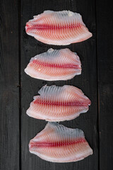 Tilapia fish skinless meat, on black wooden table, top view