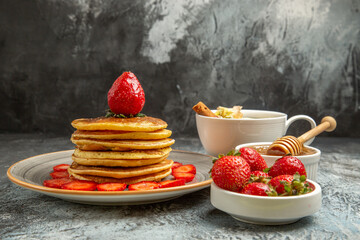 front view yummy pancakes with strawberries and cup of tea on a light background fruit cake sweet