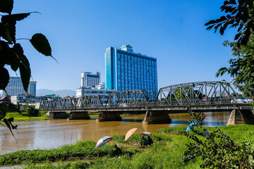 Ping River has an old iron bridge across it. There are tall buildings and ancient houses next door. In the north of Thailand ,Chaing Mai