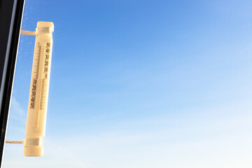 outdoor thermometer on home window (focus on the thermometer) lit by sunrise sun shows zero degrees celsius and blue sky on background on sunny winter morning