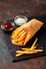 Tasty french fries with sauces on slate cutting board, on dark background