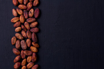 Unpeeled raw brown cocoa beans in heap lie On black modern concrete background. Flat lay, mock up, copy space. Raw materials for making cocoa powder, cocoa beverages, chocolate. Health drink concept © Ekaterina