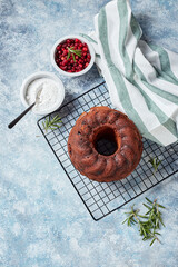 Chocolate bundt cake on a metal wire rack, powdered sugar and cranberries in bowls