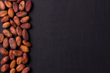 Unpeeled raw brown cocoa beans in heap lie On black modern concrete background. Flat lay, mock up, copy space. Raw materials for making cocoa powder, cocoa beverages, chocolate. Health drink concept