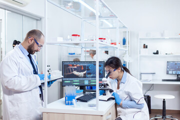 Fototapeta premium Chemist wearing safety glasses and using tablet pc in lab. Team of researchers doing pharmacology engineering in sterile laboratory for healthcare industry with african assistant in the background.