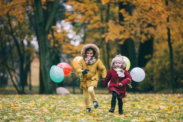 brother and sister running through an autumn park with balloons