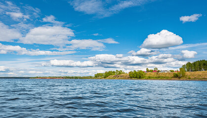 Panorama of a calm lake, the Kama River, blue sky with clouds reflected in the water. A village on the river bank.