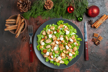top view caesar salad on oval plate fork knife bowl with dried crust xmas tree toys cinnamon sticks on dark red background