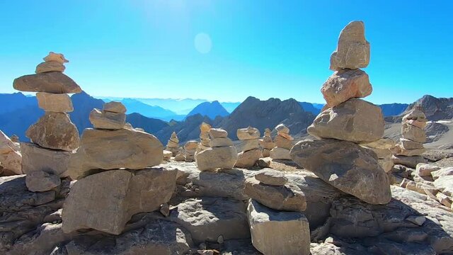 Kamerafahrt an Stein T&uuml;rmchen Haufen vor Berg Alpen Panorama mit blauem Himmel und Sonne
