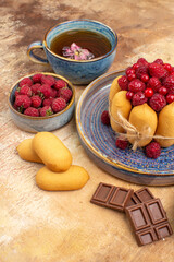 Horizontal view of hot herbal tea soft cake with fruits chocolate bars biscuits on mixed color table
