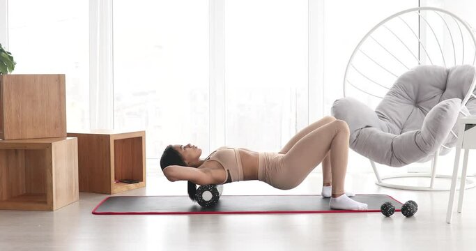 Fitness black woman in sportswear doing fitness using foam roller. Exercises on yoga mat with roller at home on living room.