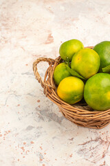 Vertical view of fresh tangerines in a wooden basket on mixed color background