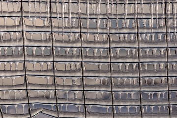 Ice rain series: icicle on a grid-fence on sky background close-up