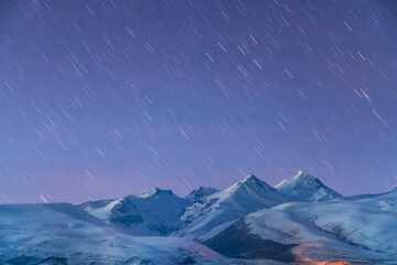 Beautiful night winter landscape. The mountain peaks snow-covered. Starry sky, night photography.