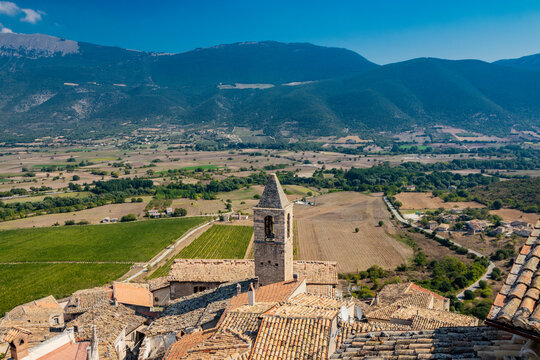 The ancient medieval village of Capestrano seen from the top of the castle. The tiled roofs of the houses, the bell tower, the valley with the cultivated fields and the green mountains in background.