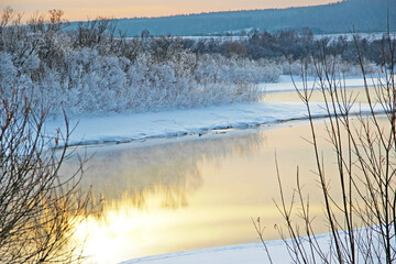 Winter river runs between snowy shores and the sky reflection creates just fantastic landscape.